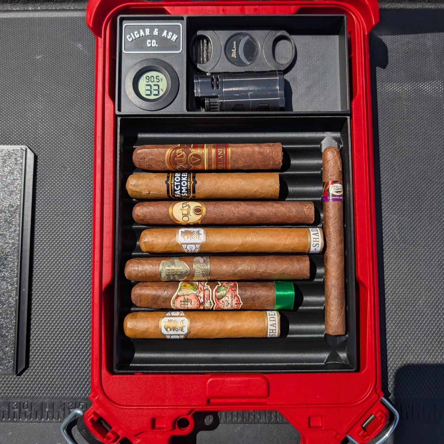 Cigar & Ash Co. Packidor travel humidor insert filled with premium cigars, digital hygrometer, lighter, and cutter inside a red Milwaukee Packout case.