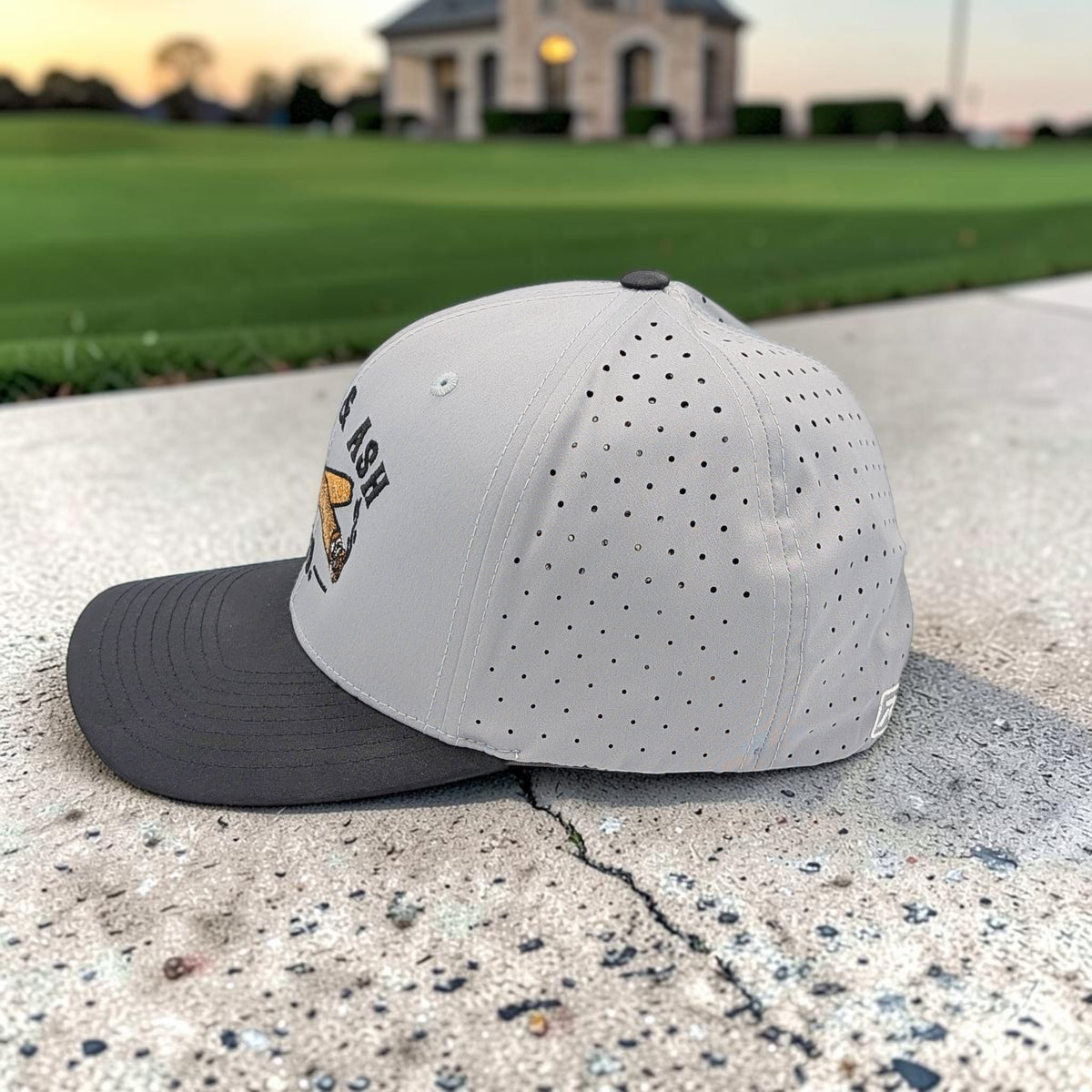 Side view of Cigar & Ash Co. two-tone grey and black performance snapback hat highlighting laser perforated airflow panels
